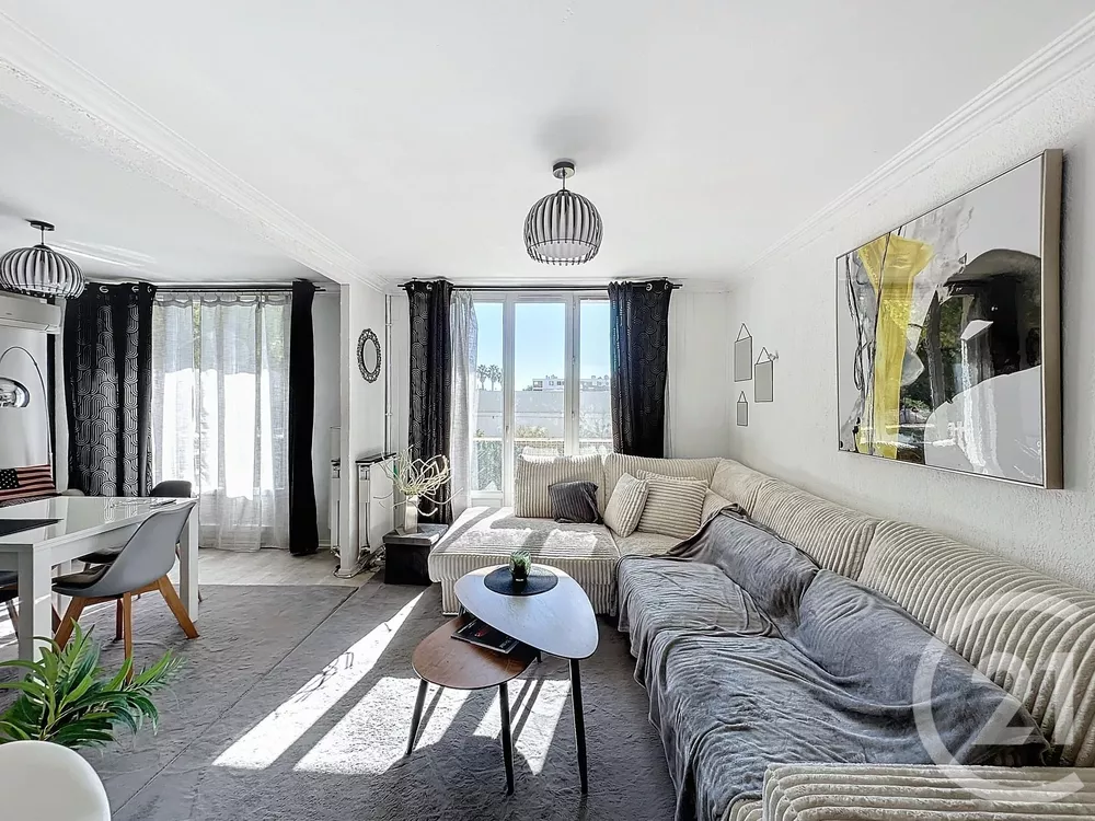 Séjour lumineux avec grand canapé d'angle beige, rideaux noirs, table basse en bois et décoration murale moderne